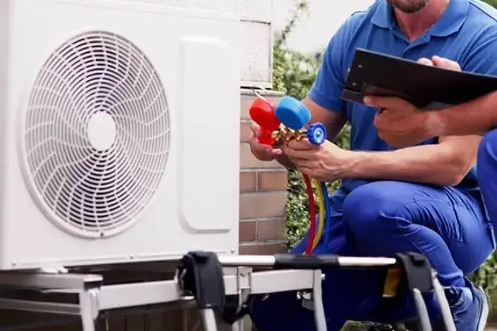 An engineer checking the refrigerant gauges on an outdoor air source heat pump unit